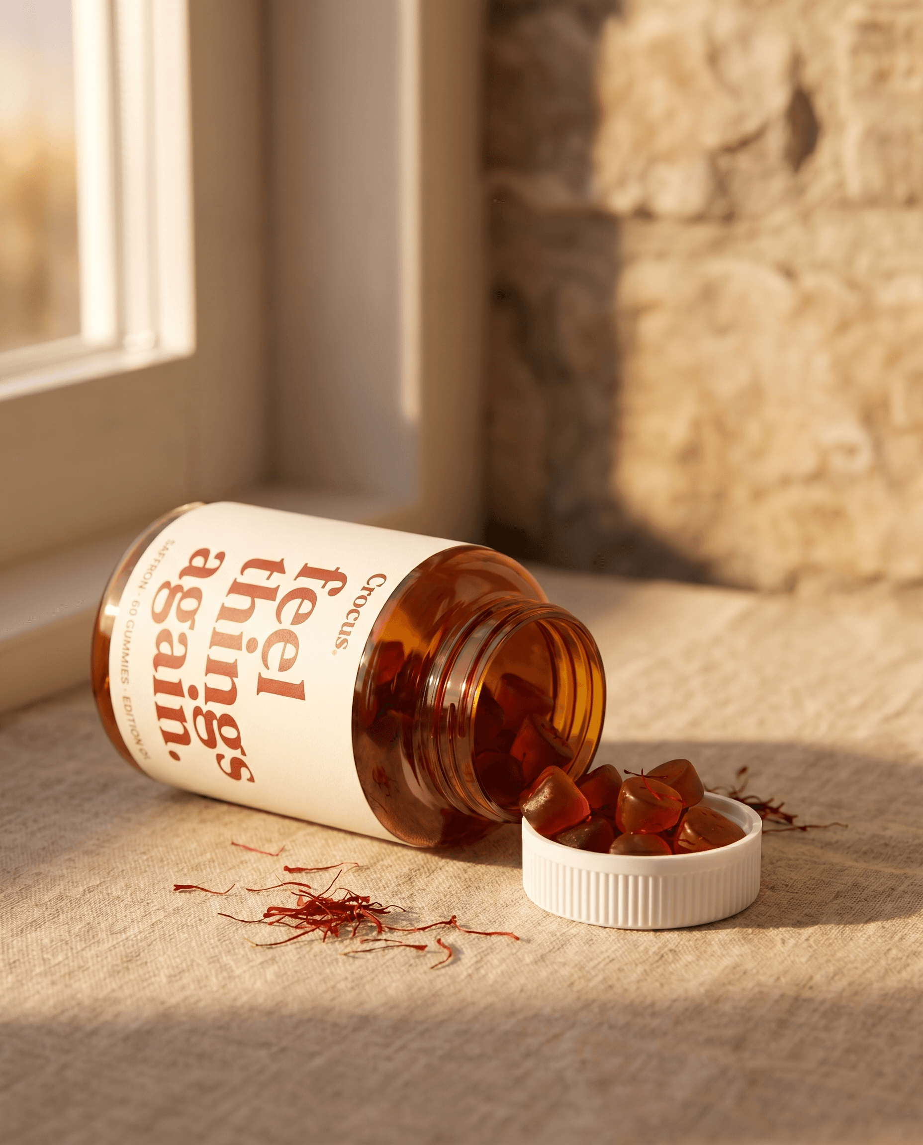 Crocus Spark jar tipped on its side with amber gummies and saffron threads spilling onto warm linen in golden window light